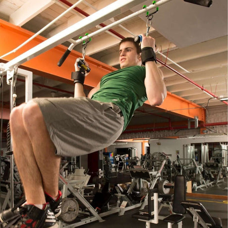 Man does a pull-up in a gym, wearing a green shirt and gray shorts, with workout equipment in the background.