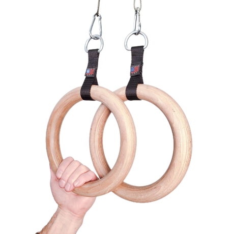 A hand grips the Gymnastic Rings Cable Machine Handles for Roman Ring Workout—sturdy wood rings with black straps and metal clips, highlighting the strength and elegance of this gym rings pair.
