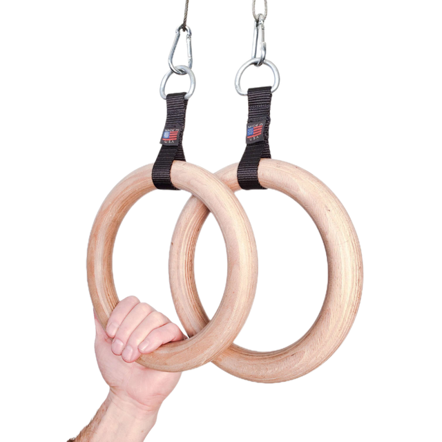 A hand grips the Gymnastic Rings Cable Machine Handles for Roman Ring Workout—sturdy wood rings with black straps and metal clips, highlighting the strength and elegance of this gym rings pair.