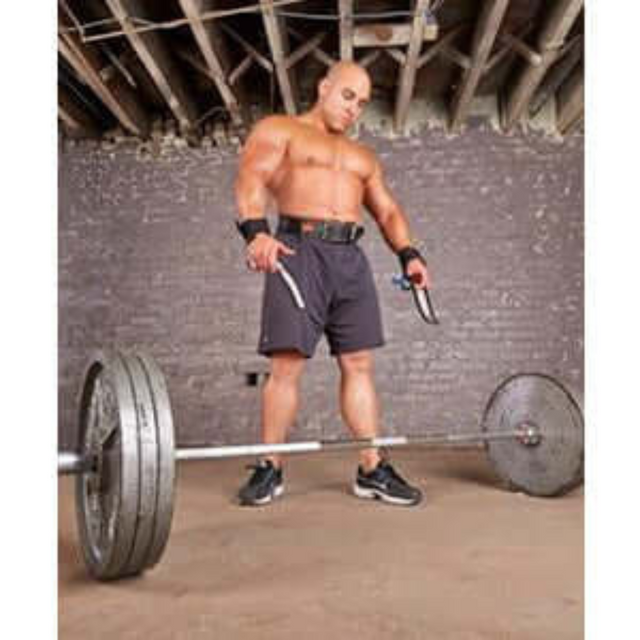 A man in gym attire, wearing HAULIN HOOKS 'PROFESSIONAL' neoprene wrist support, confidently stands before a barbell in a basement with exposed beams, ready for deadlifts.