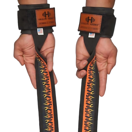 Two hands wear HAULIN HOOKS 'STRAPS 1000' black heavy-duty lifting straps with flame designs and labels, offering perfect grip and support for deadlifts.