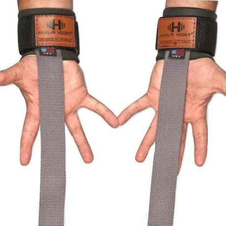 Hands presenting USA-made HAULIN HOOKS 'STRAP 650' lifting straps featuring gray fabric, leather patches, and neoprene wrist padding for optimal comfort.