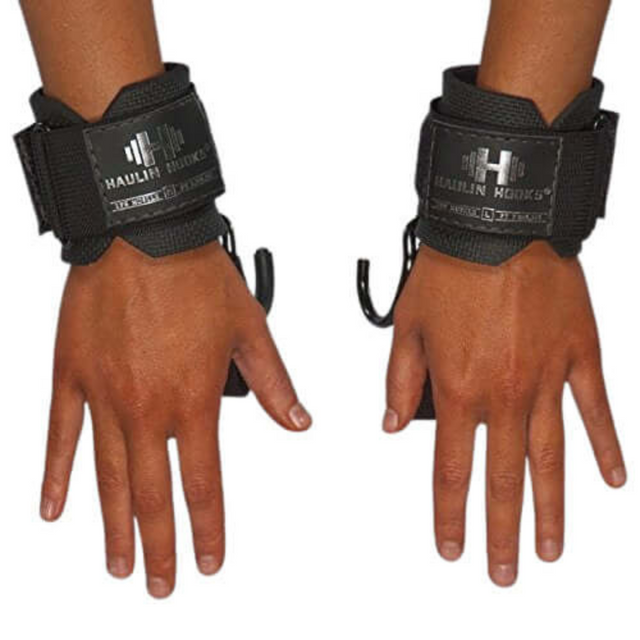 A fitness-dedicated woman wears HAULIN HOOKS 'WOMENS' black lifting straps with metal hooks for weightlifting, her open hands and palms facing down, showcasing readiness and strength.