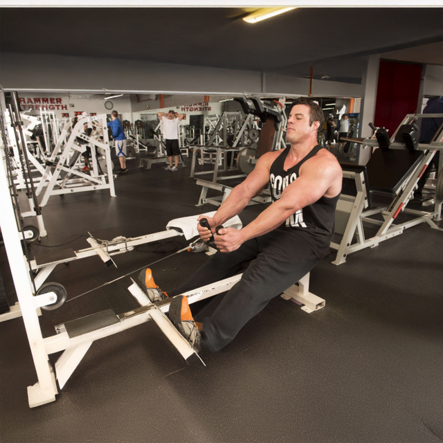 A man in a gym uses the HOG LEGS 'multi-row' Low Pulley Cable Row Handles Plus with Pull Up Hook & Snap Link, surrounded by other exercise equipment and people doing pull-ups and T-Bar Row exercises.