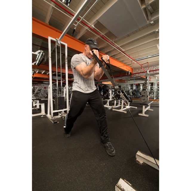 In a gym, a man wearing a cap, grey shirt, and black pants is focused on resistance band exercises using DELT-BELT Handle Straps for Cable Machine Upright Rows, offering an effective dumbbell alternative for precise muscle targeting.