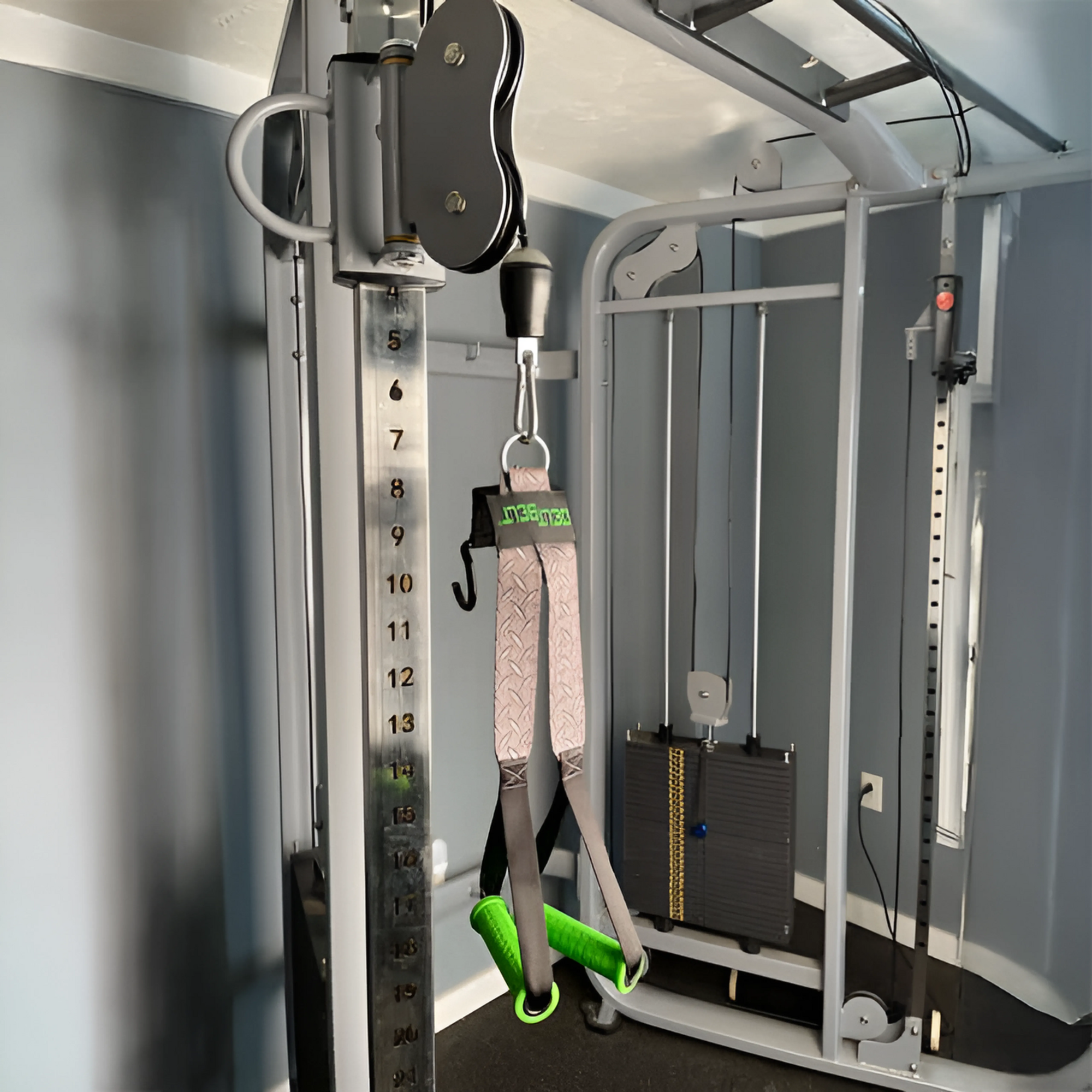 Close-up of a cable machine with DELT-BELT Handle Straps for Cable Machine Upright Rows plus! in a home gym with gray walls, ideal for exercises like the Dumbbell Upright Row.