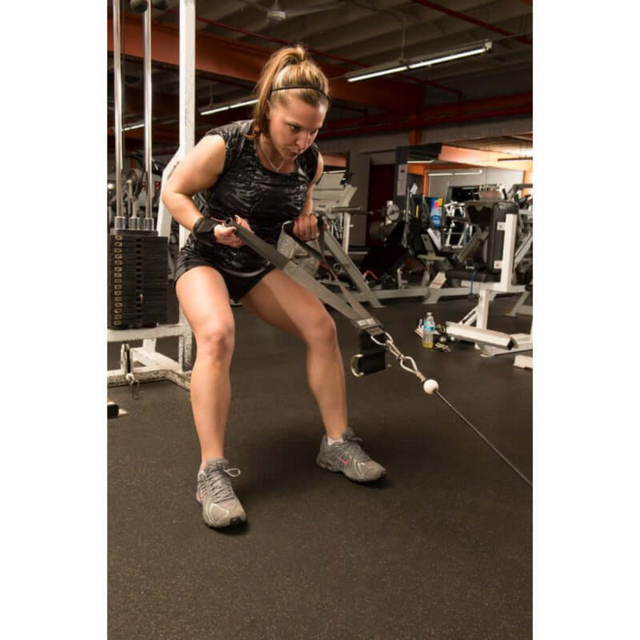 A woman in a gym uses DELT-BELT Handle Straps for cable machine upright rows, wearing athletic clothes and focusing on muscle targeting for an effective workout.