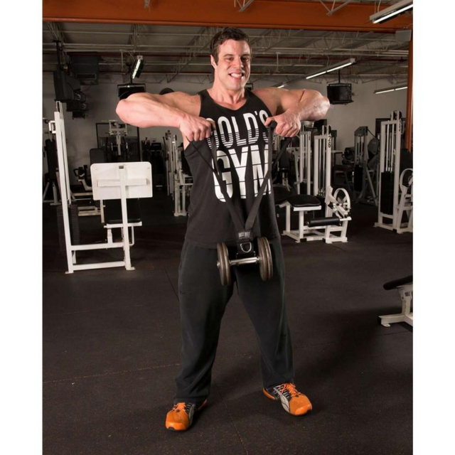 In the gym, a man demonstrates an exercise using a DELT-BELT Handle Strap for cable machine upright rows. Focused on muscle targeting, he wears a sleek black tank top and eye-catching orange shoes.