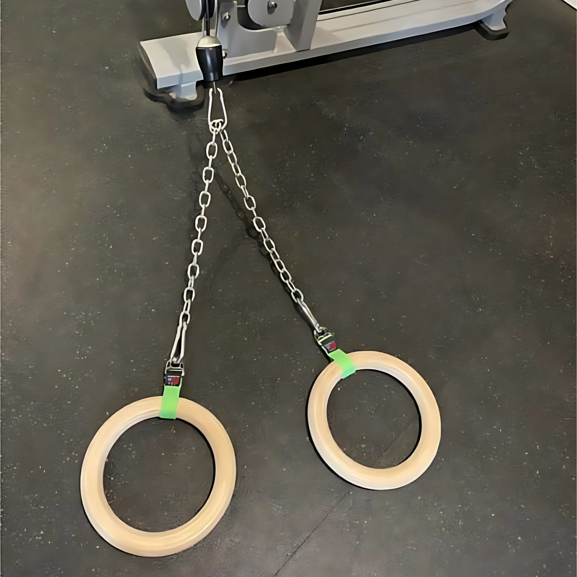 A pair of Gymnastic Rings Cable Machine Handles for Roman Ring Workout hangs from sturdy metal chains on a black gym floor.