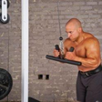 A man works his triceps with the HOG LEGS 'Arm Yourself' Cable Machine Attachments Set, featuring a durable FAT 1 3/4″ round welded steel grip, set against a rugged brick wall backdrop at the gym.