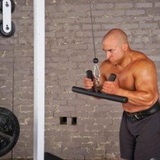 A man works his triceps with the HOG LEGS 'Arm Yourself' Cable Machine Attachments Set, featuring a durable FAT 1 3/4″ round welded steel grip, set against a rugged brick wall backdrop at the gym.