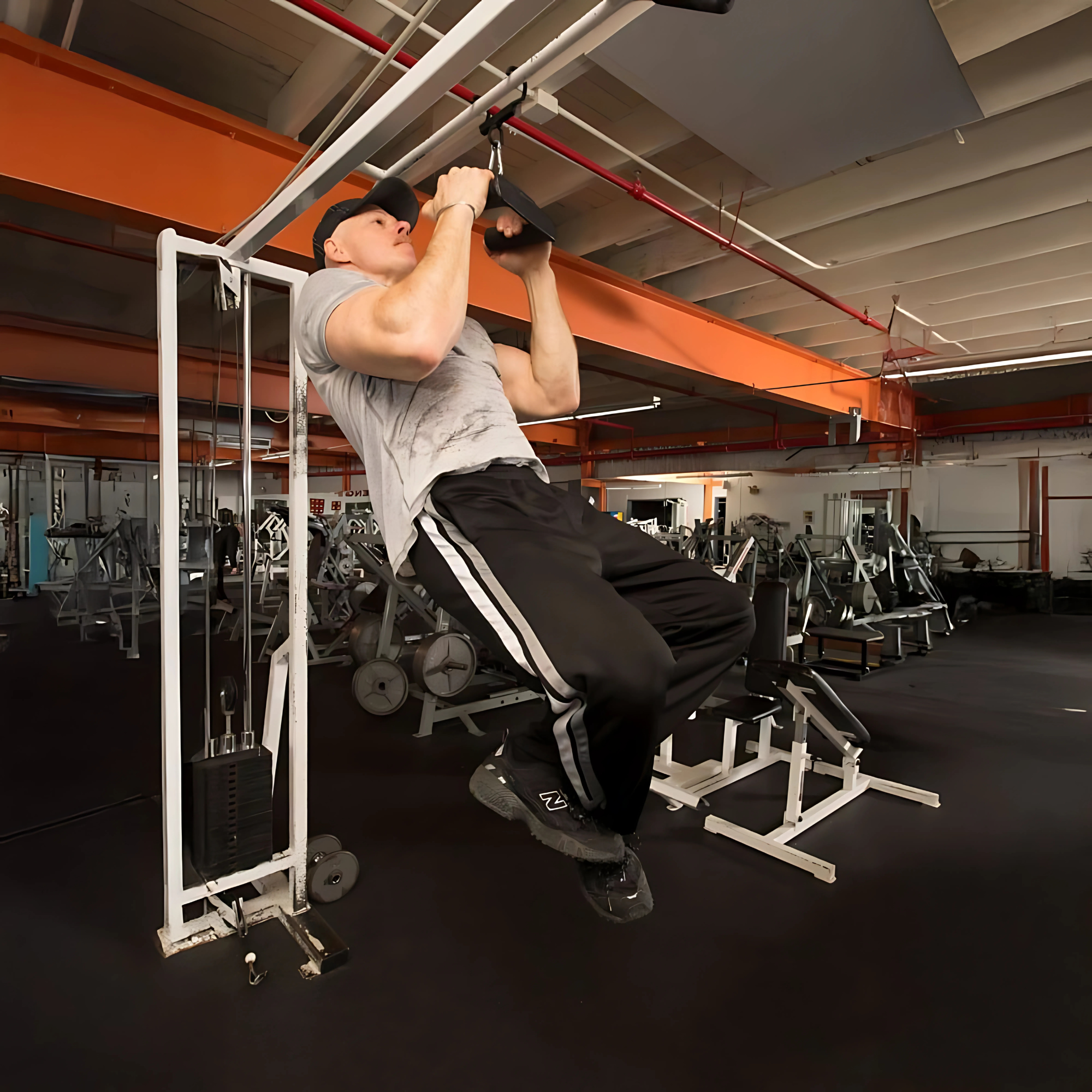 A man in a gray shirt and black pants does pull-ups in the gym, with the HOG LEGS 'Back Pac' LEGIT Cable Machine Attachments Set, including items like the lat bar, visible nearby.