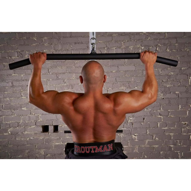 A man highlights his strong back muscles using the USA-made HOG LEGS 'Back Pac' LEGIT cable machine attachments set on a bar, positioned against a brick wall.