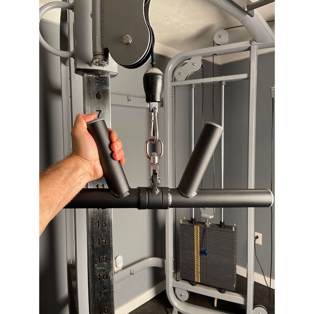 A hand grips the HOG LEGS 'Boar Tusk' Fat Grip Curling Bar for triceps cable exercises, highlighting forearms amid an energetic backdrop of weights and gym equipment.