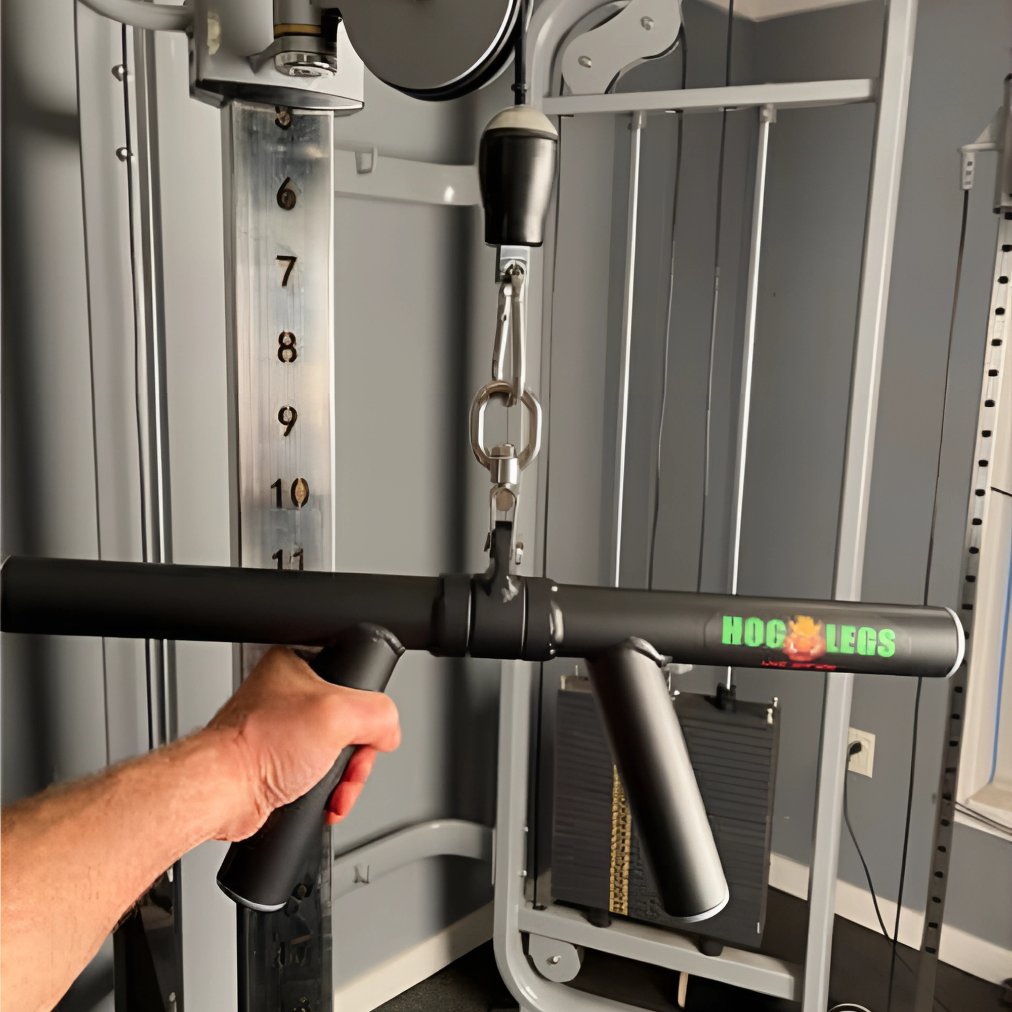 A person holds the HOG LEGS 'Boar Tusk' Fat Grip Curling Bar for triceps cable exercises in front of a gym machine, ready to work their biceps and triceps.