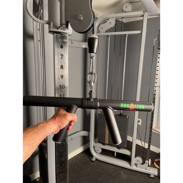 A hand grips gym equipment with a HOG LEGS 'Boar Tusk' Fat Grip Curling Bar on a cable machine, focusing on triceps and forearms, as the weight stack is visible in the background.