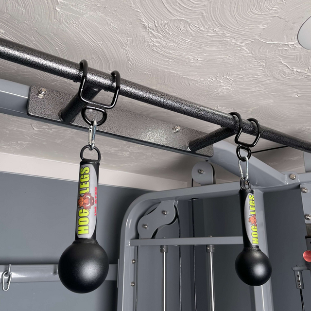 Two black "HOG LEGS 'Fist Full' Pullup Handles & Tricep Attachment" dangle from a metal pull-up bar in a home gym, enhancing grip strength for challenging workouts.