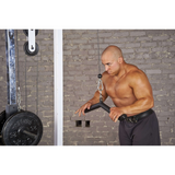 A man intensely works out on a cable machine against a gray brick wall, using the HOG LEGS 'Hog Wild' Workout Cable Attachments gone Fat! for enhanced muscle stimulation.