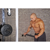 In a gym with gray brick walls, a man intensely focuses on his workout, using HOG LEGS 'Hog Wild' Workout Cable Attachments gone Fat! on the cable machine to maximize muscle stimulation.