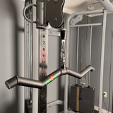 Close-up of a gym machine showcasing HOG LEGS 'Hog Wild' Workout Cable Attachments featuring a handlebar, weight stack, and cables designed for muscle stimulation against a gray wall.
