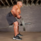A muscular man in gym shorts uses the HOG LEGS Hog Balls Upper Body Exercise Equipment Bar for bent-over rows in an industrial gym, focusing on optimal muscle recruitment during his upper body workout.