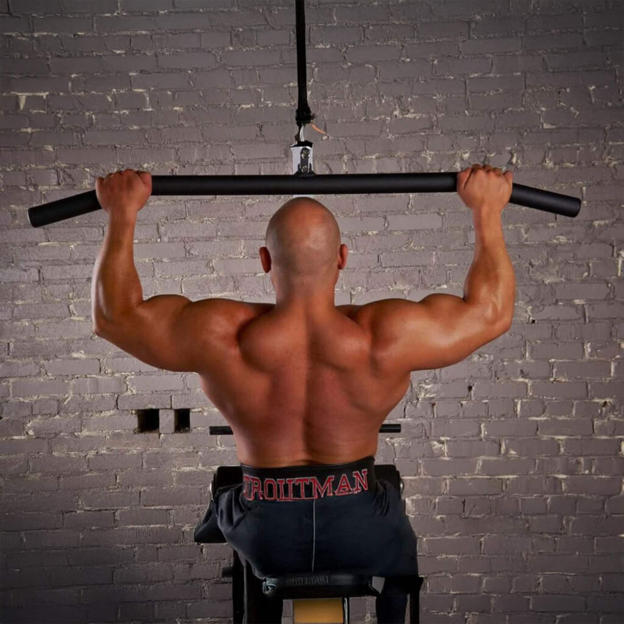 A muscular man uses HOG LEGS 'Hog Wild' Workout Cable Attachments gone Fat! for a lat pulldown in front of a gray brick wall, enhancing muscle activation with premium equipment.