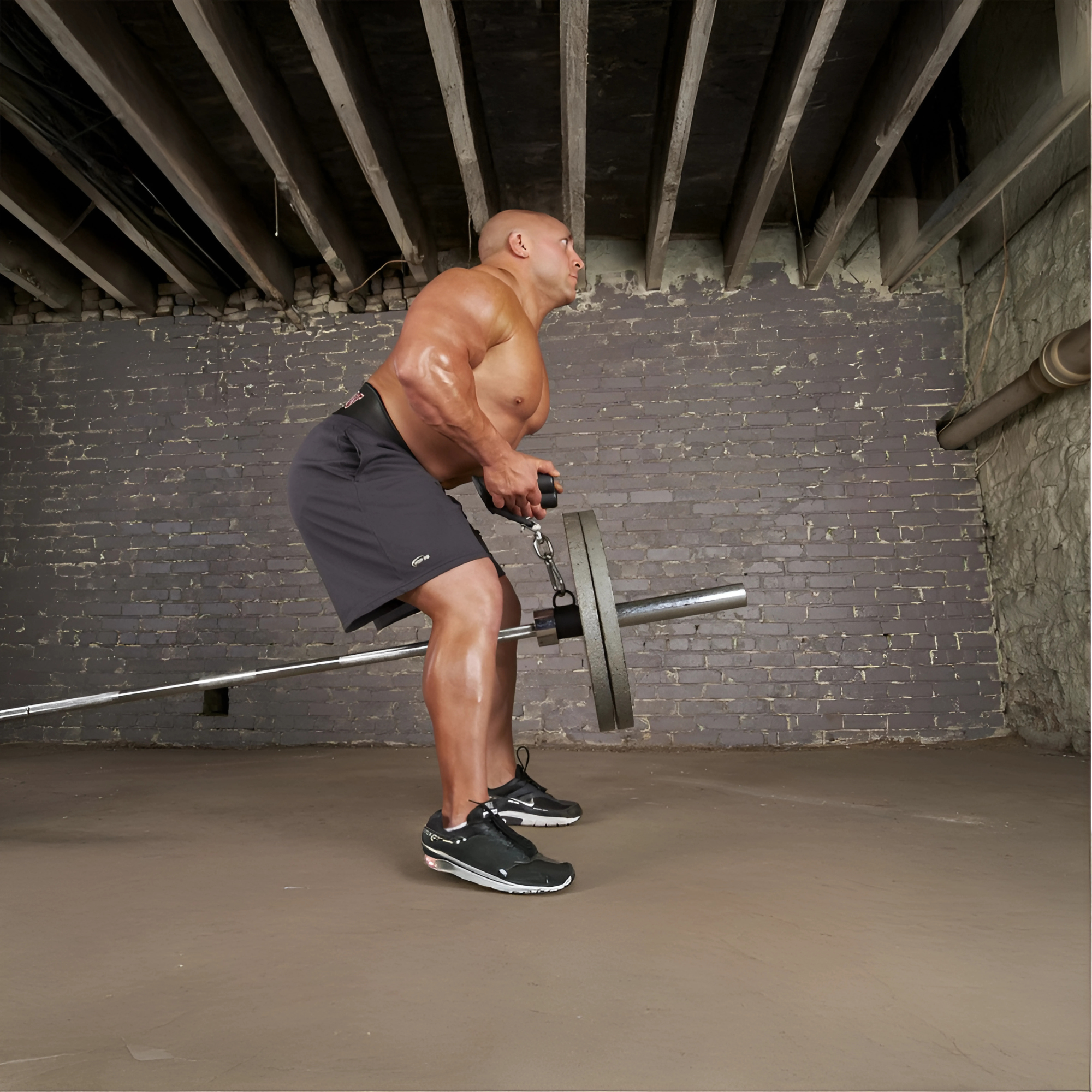 A muscular man uses the HOG LEGS Landmine Olympic T-Bar Row Handles Attachment Ring for bent-over rows in a basement gym with exposed beams and brick walls.