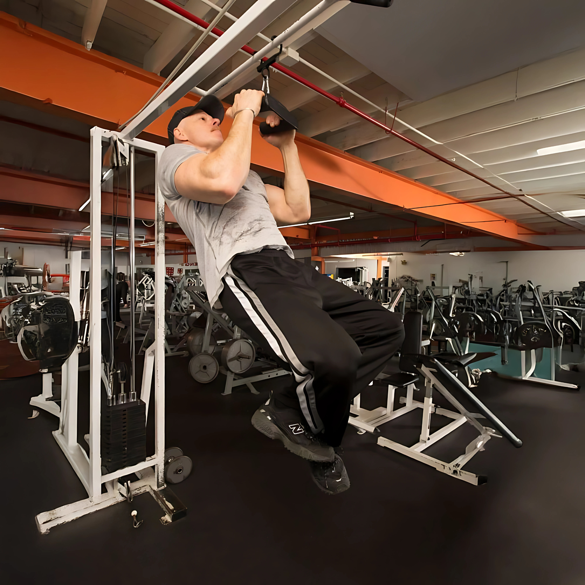 Man performing pull-ups on HOG LEGS 'multi-row' Low Pulley Cable Row Handles Plus with Pull Up Hook & Snap Link, wearing a grey shirt and black pants, in a fitness center equipped for pull-ups and T-BAR ROW exercises.