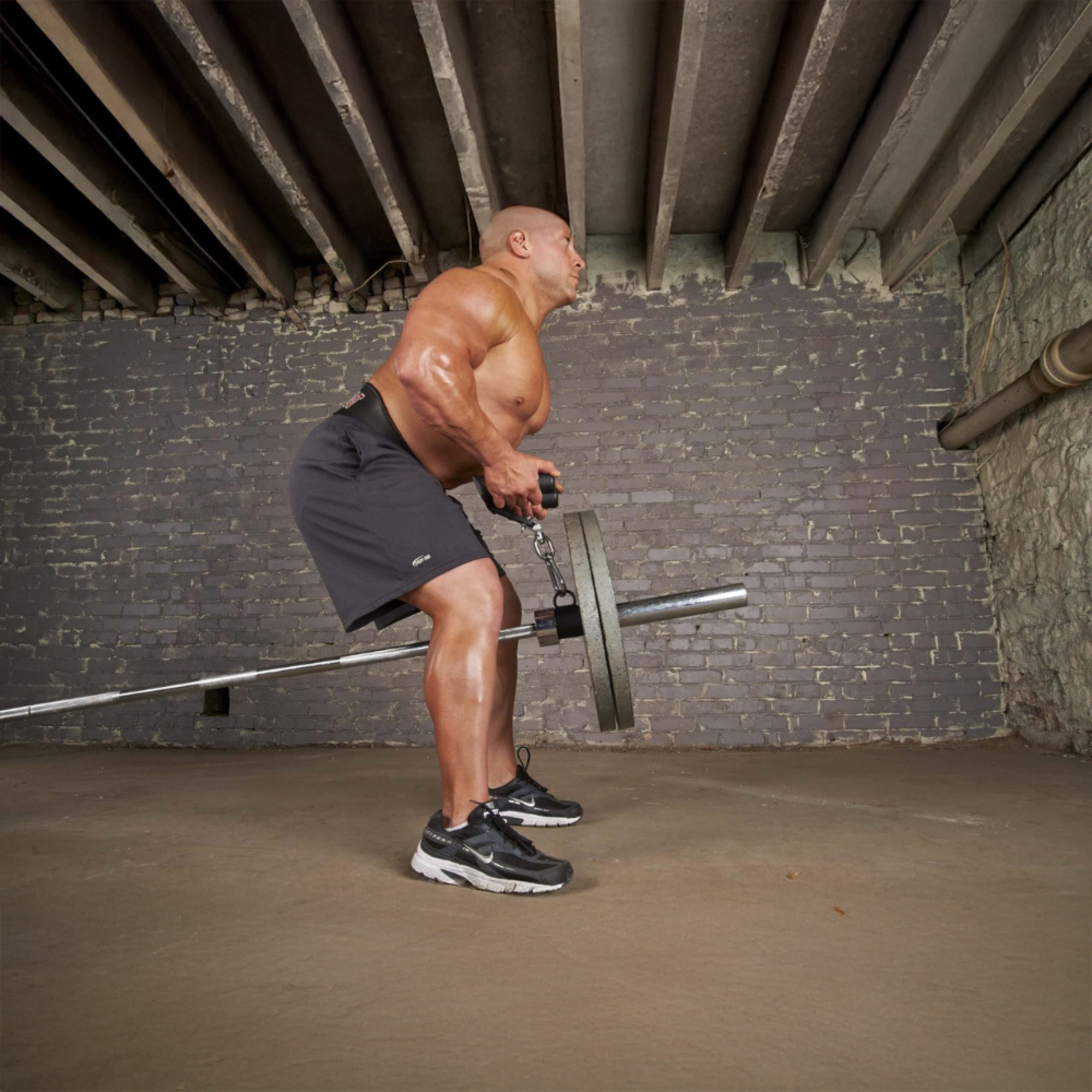 A muscular man uses HOG LEGS 'multi-row' Low Pulley Cable Row Handles Plus with Pull Up Hook & Snap Link to perform a T-Bar Row in a gym with concrete walls and exposed beams.