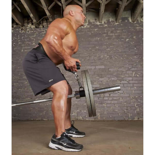 A man in the gym demonstrates strength and determination as he lifts a weighted barbell with chains. Dressed in black shorts and sneakers, he stands against a brick wall with HOG LEGS Multi-Row 'Wide' Back Cable Exercise Handles nearby to enhance his workout.