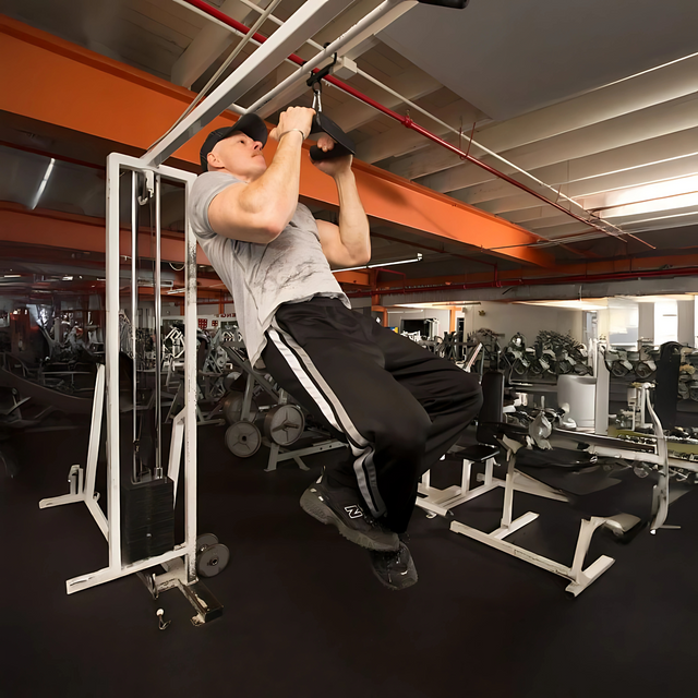 Man doing a pull-up on HOG LEGS Pull Up Handles Hook in a gym, wearing a gray shirt, black pants, and a black cap.