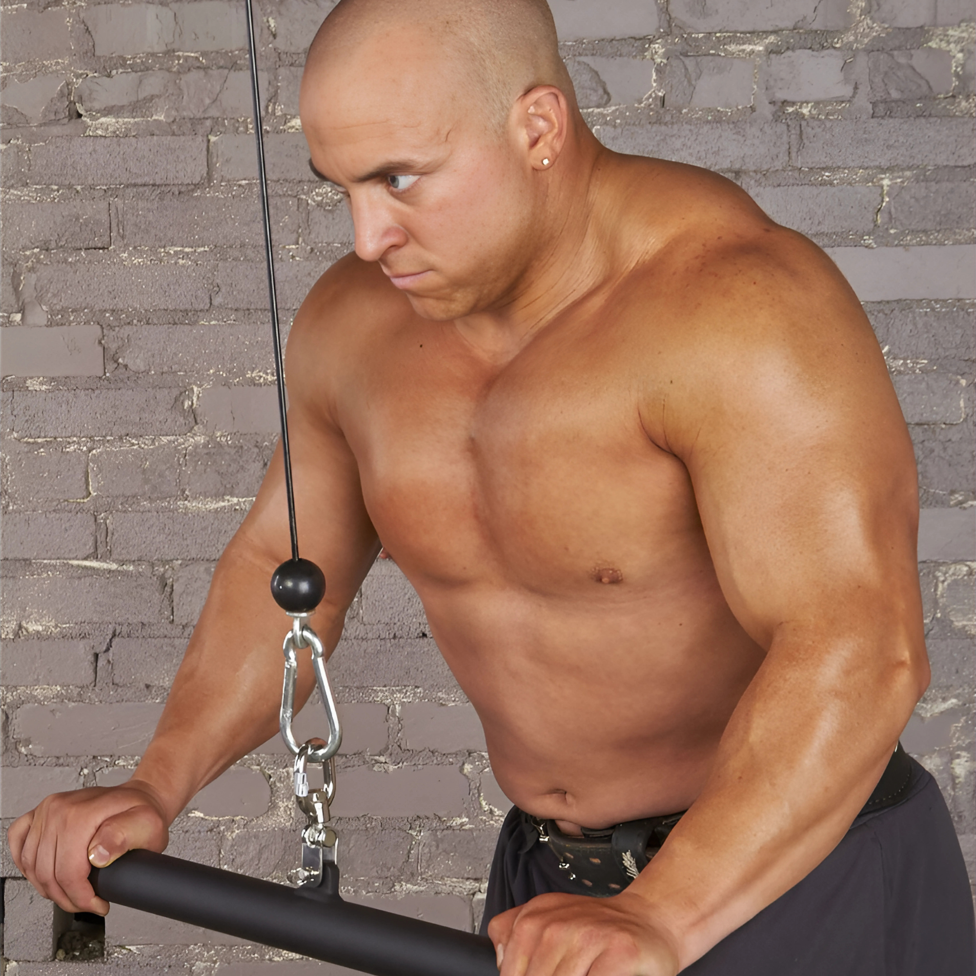 A muscular man uses the HOG LEGS 'Revolution' Fat Grip straight Curling Bar Gym Cable Attachment, featuring a non-slip gripping surface for enhanced muscle activation, against a gray brick wall background.