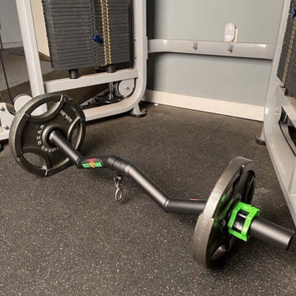 The HOG LEGS Super Subprimal Cable & Olympic Easy Curl Bar is positioned on the gym floor, surrounded by workout equipment and mirrors, next to an Olympic free weight.