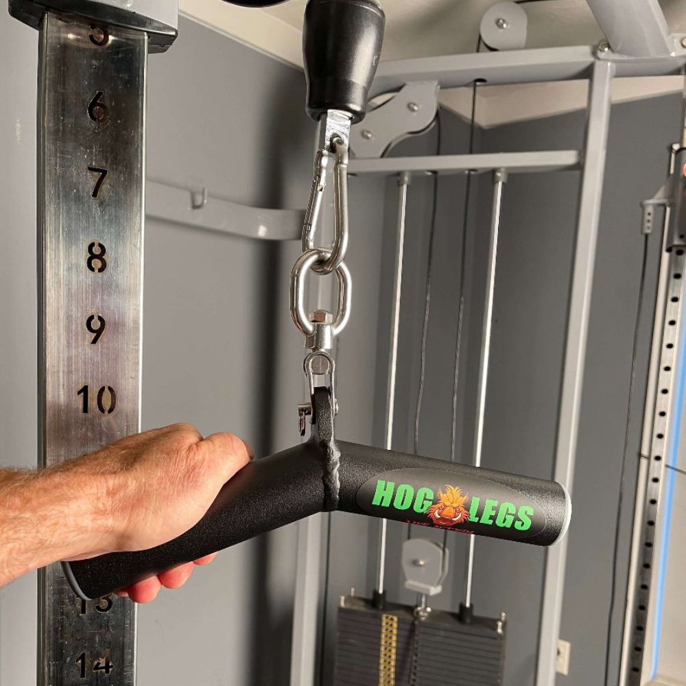 A hand grasps a "HOG LEGS Wicked 'Piglet' Tricep Bar Workout gone FAT!" attached to a pulley machine, weight markers in view, guaranteeing precise triceps targeting and enhanced muscle stimulation.