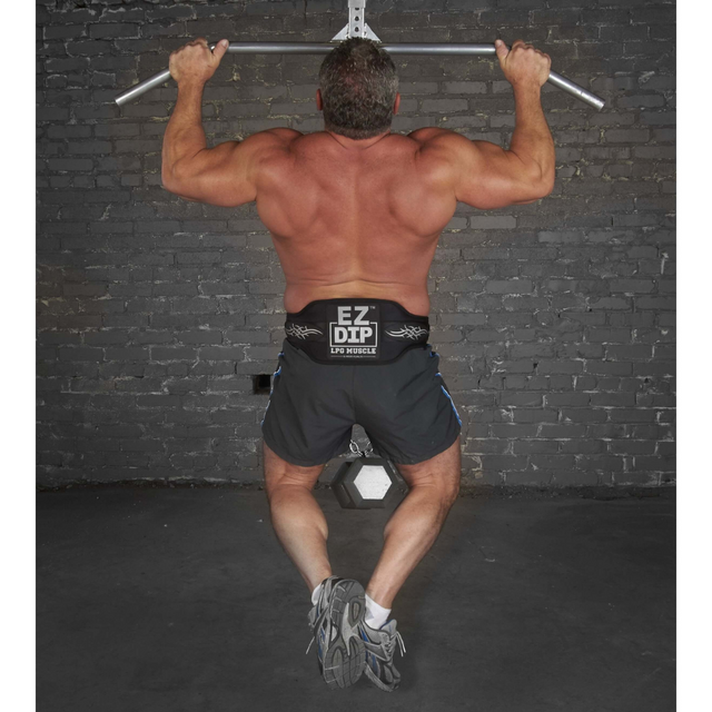 A man, clad in shorts and sneakers, performs a pull-up at the gym. He showcases strength and determination with the LOADING PIN for Weights plus Dip Belt with chain HOOK strapped around his waist, facing a brick wall.