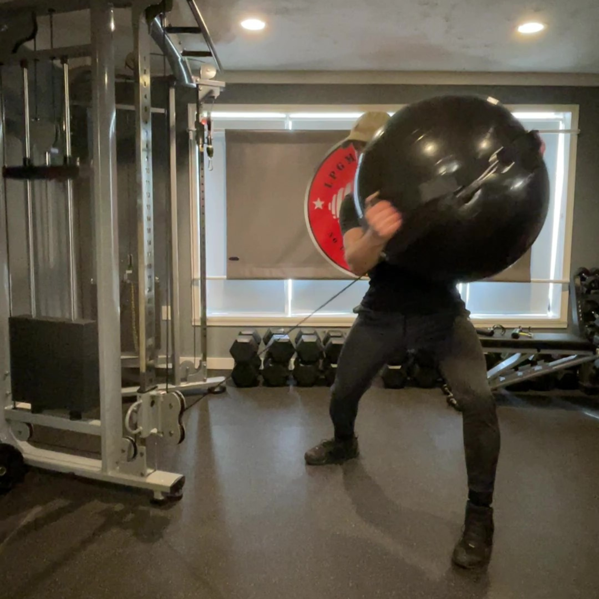 In the gym, a person stands with legs apart near weights, holding the PHYSIO TWIST Swiss Ball Handle Straps for Cable Machine Core, ready to build explosive core power.