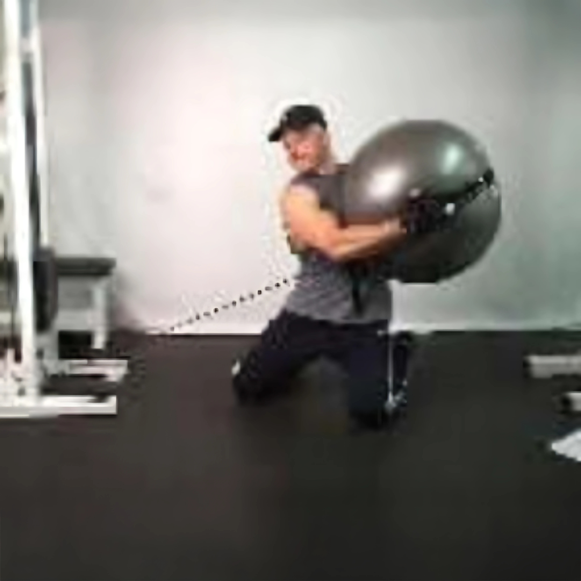 Person kneeling on the gym floor, performing a core-strengthening Physio Twist using the PHYSIO TWIST Swiss Ball Handle Straps for Cable Machine Core—an explosive move targeting core muscles.