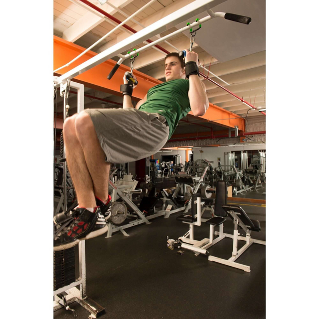 A man in a green shirt and gray shorts uses PULL FORCE 'Freestyle Motion' Rotating Pull Up Grips and wrist straps for support to perform pull-ups.