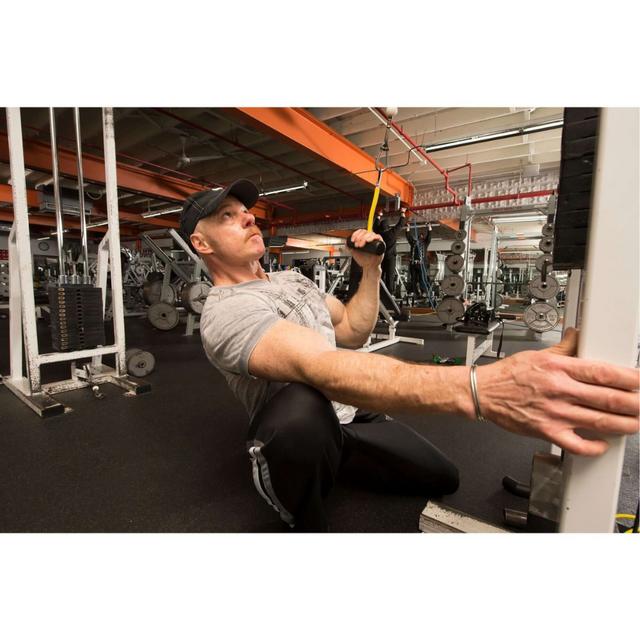 Using the PULL FORCE GEN2 Cable Machine Back Workouts Single Grip, someone kneels to adjust the weights meticulously for an optimal back workout.