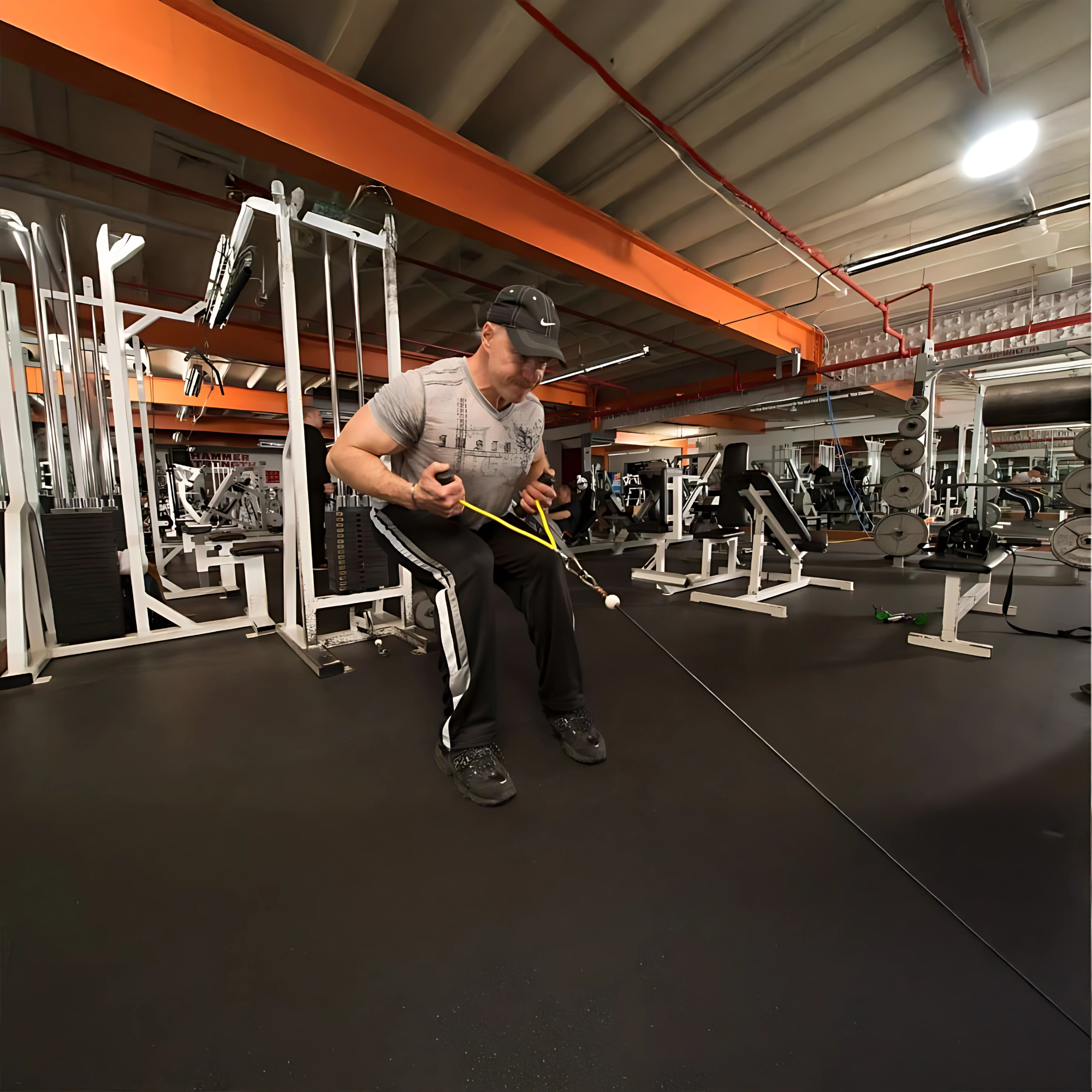 Man exercising with a seated cable row machine using the PULL FORCE GEN 2 Double Grips Cable Gym Attachment in a spacious gym filled with various fitness equipment.