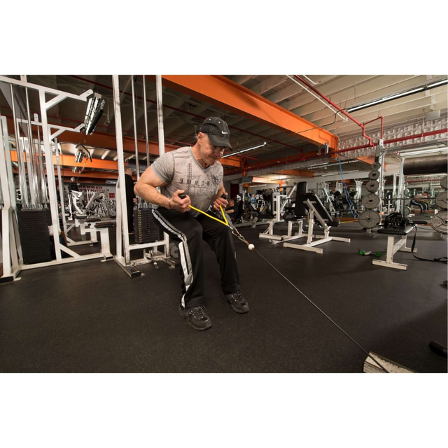 A man in a gray shirt and cap works out at the gym on a rowing machine, using the PULL FORCE GEN 2 Double Grip Exercise Cable Attachments for enhanced control as he navigates between equipment with precision and focus.