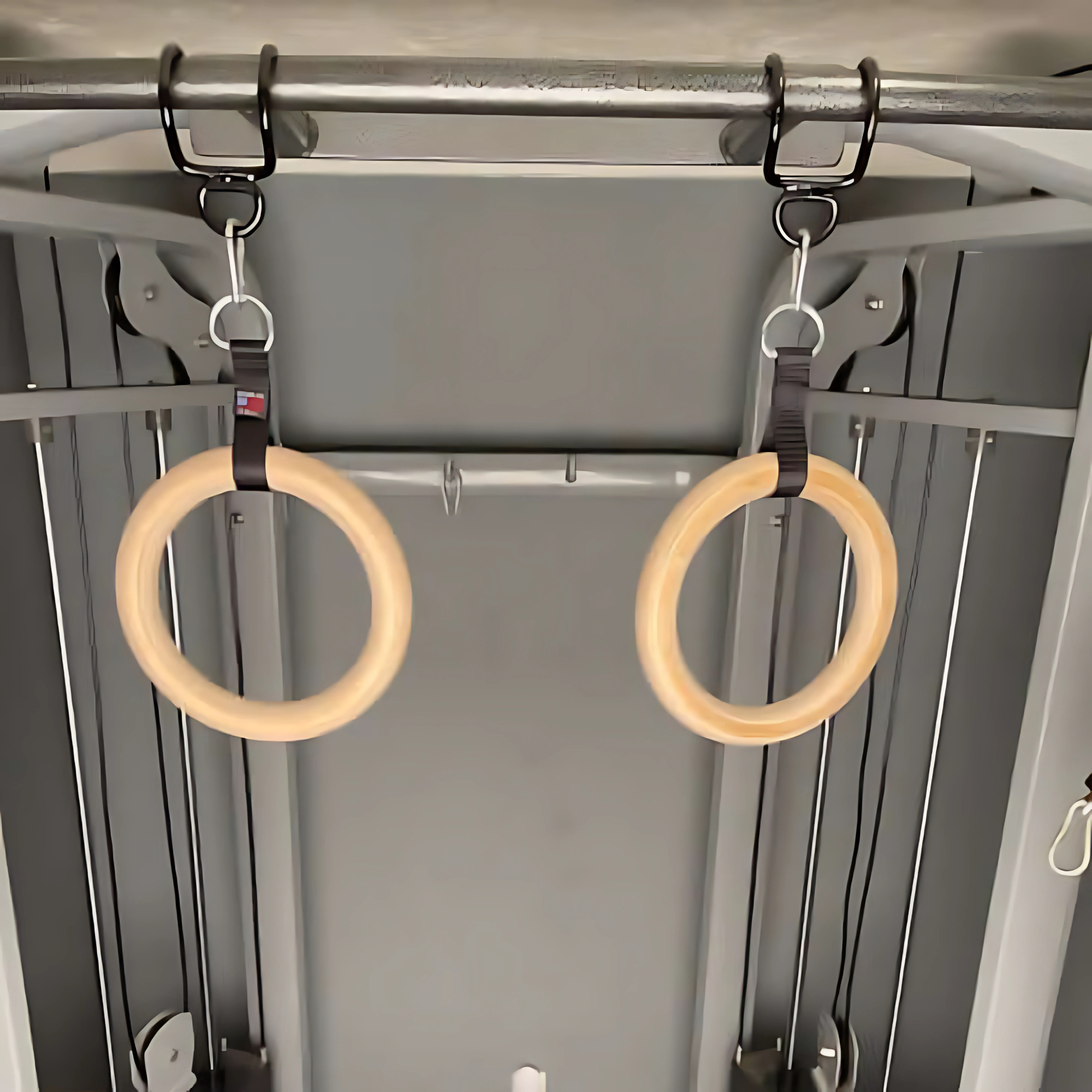 Two commercial grade wooden gymnastic rings hang from straps attached to the PULL UP BAR WORKOUT 'Extreme pack' by LPGmuscle, a metal workout station with an integrated pull up bar.