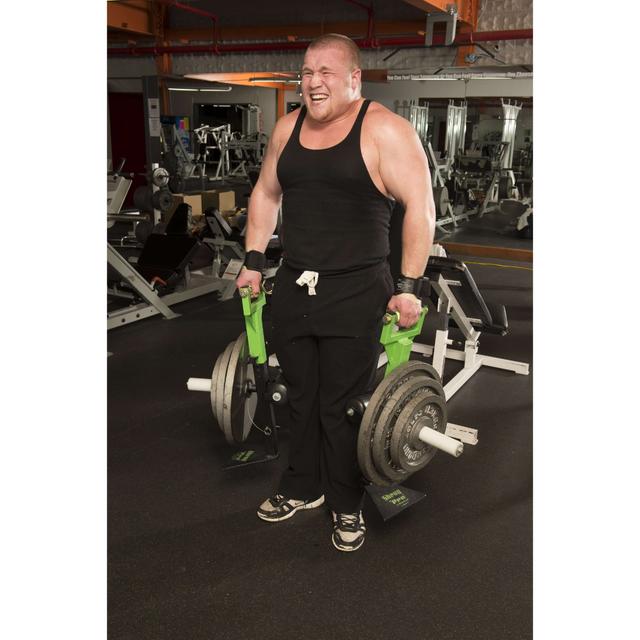 In a gym, a man in a black tank top and sweatpants lifts heavy weights with the 'SHRUG PRO' Freestanding Hex Bars Trap Bar. His strained expression shows the intense effort he's putting into mastering his workout.
