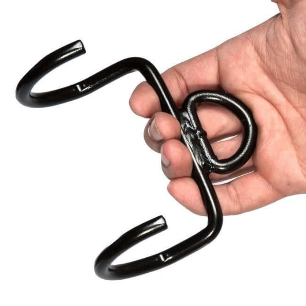 A hand holds a black TRD 'Dynamic Action' Yoke Triceps Attachment Gym Handle, featuring interlocking curved hooks like those found on typical cable machine grips.