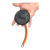 A hand grips a TRIBELLS 4" 'Hi-Tech' Cable Tricep Attachment, featuring a round black design similar to tricep ropes, with an orange flexible tail and a circular metal loop at the end.