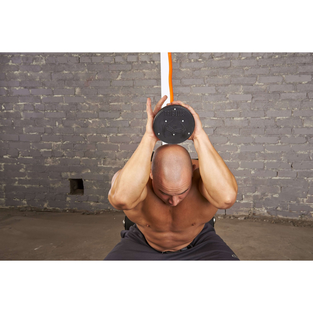 A man works out against a brick wall using the TRIBELLS 6" Palms Grip Tricep attachment, holding it above his head for an intense tricep session.