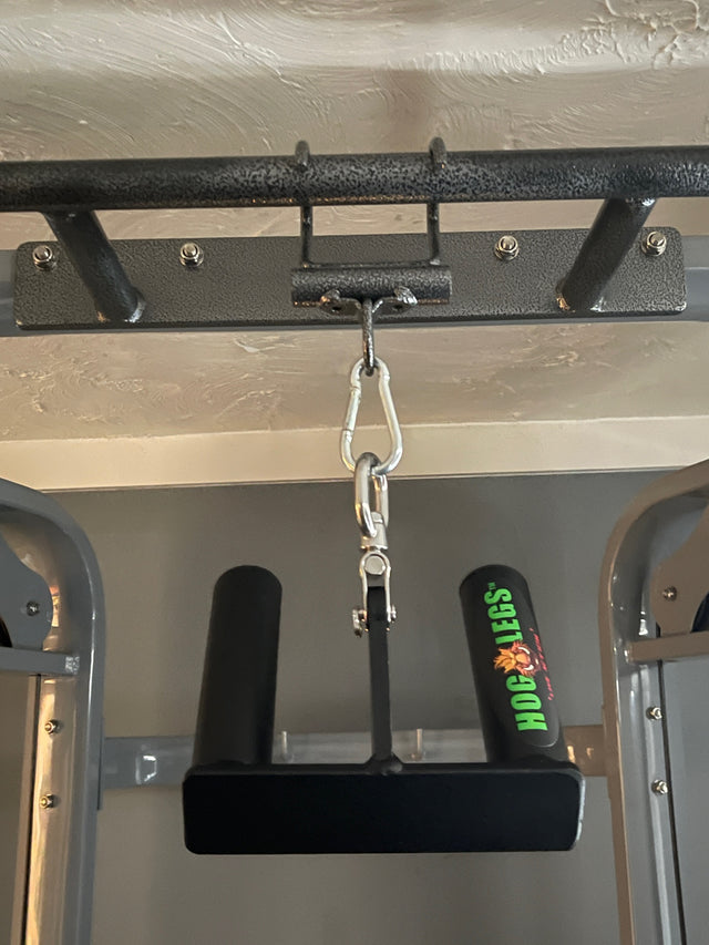 Close-up of HOG LEGS Pull Up Hooks for Exercise Cable Attachments connected by a carabiner to a gym bar, ideal for enhancing grip strength. Wall and ceiling visible in the background.